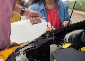 Close-up of a person pouring windshield washer fluid into a car, emphasizing vehicle maintenance.